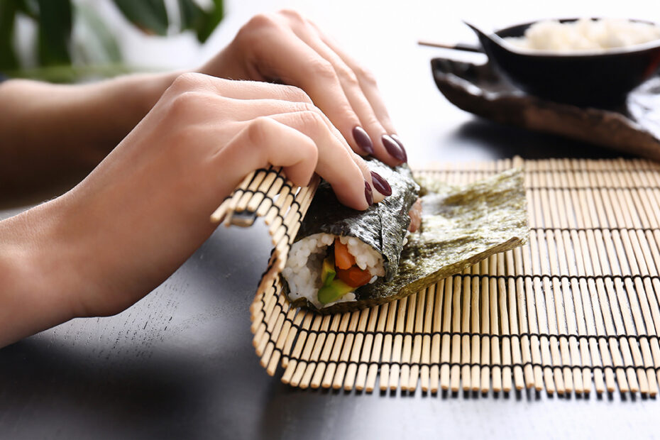 close up on hands of woman making sushi roll
