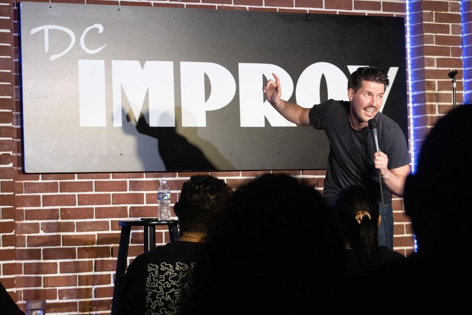 comedian on stage in front of a brick wall and "dc improv" sign