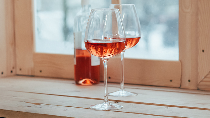 A half full bottle of rose wine and two filled glasses standing on a wooden window sill